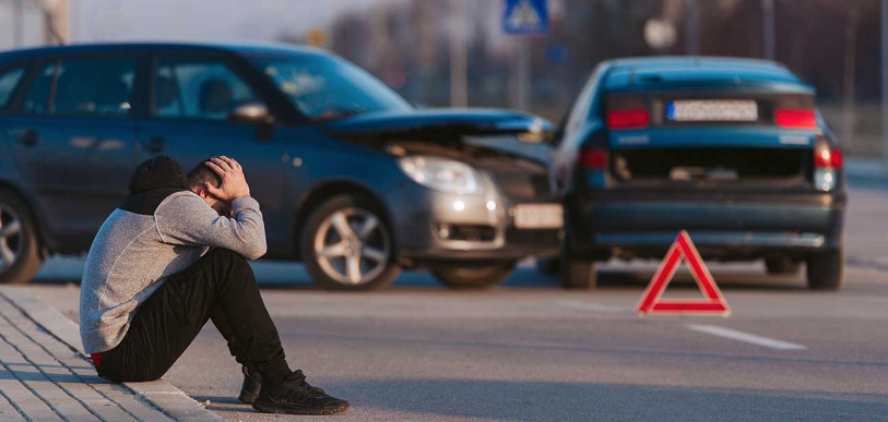 man sitting on curb at scene of car crash